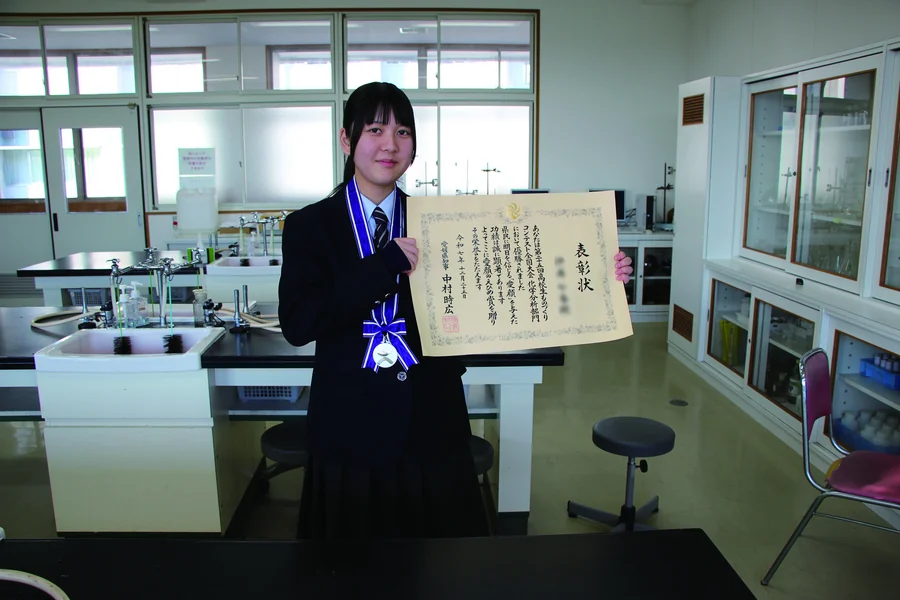 表彰状を手に実験室で立つ生徒