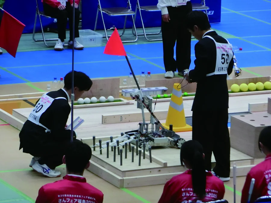 競技フィールドでロボットを操作する生徒たち