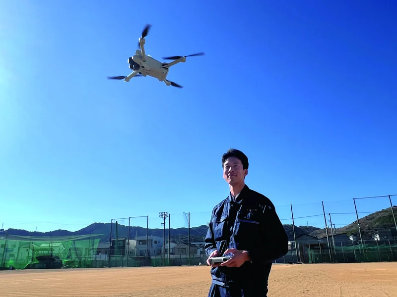 校庭でドローンを操縦する生徒と、青空を飛ぶドローン