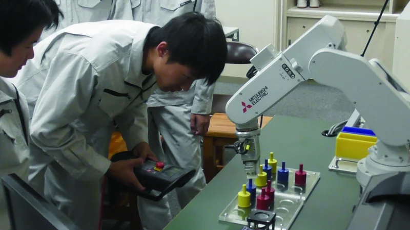 ティーチングペンダントでロボットアームを操作する生徒